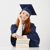 Dreamy graduate girl smiling thinking sitting with books. Copy space.