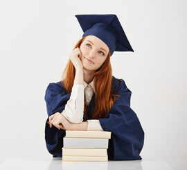 Dreamy graduate girl smiling thinking sitting with books. Copy space.